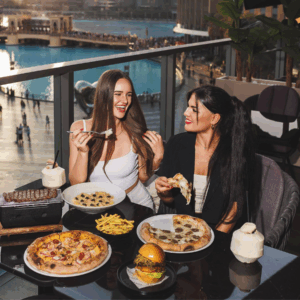 Two women enjoying pizza, pasta, fries, and a burger