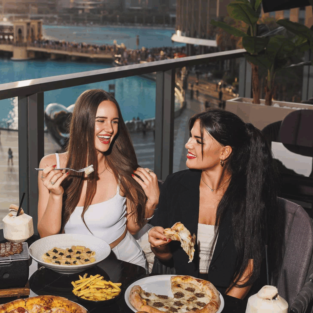 Two women enjoying pizza, pasta, fries, and a burger