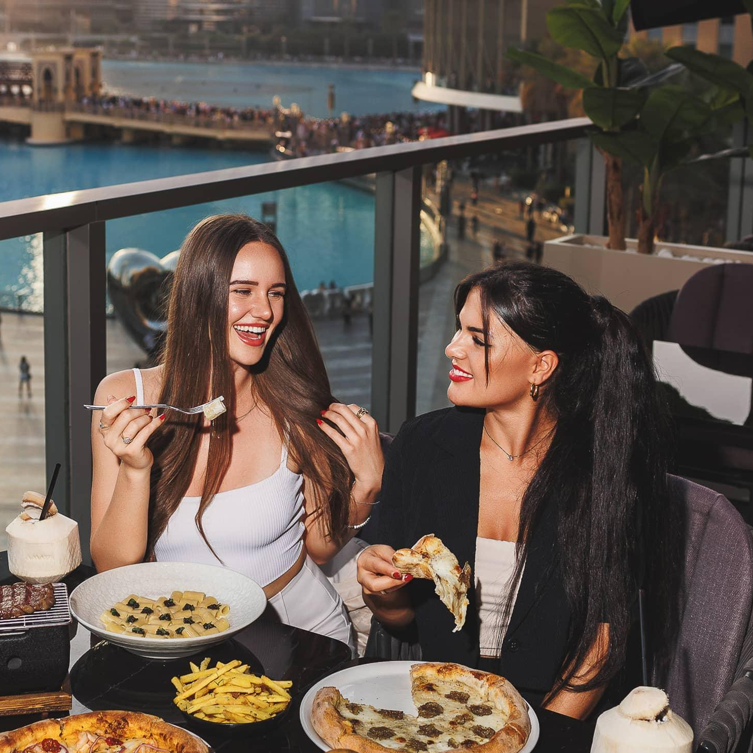 Two women enjoying pizza, pasta, fries, and a burger