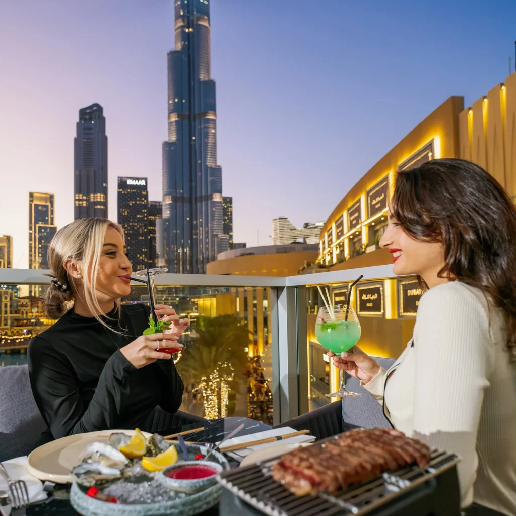 Two women sipping on drinks with the Dubai evening view