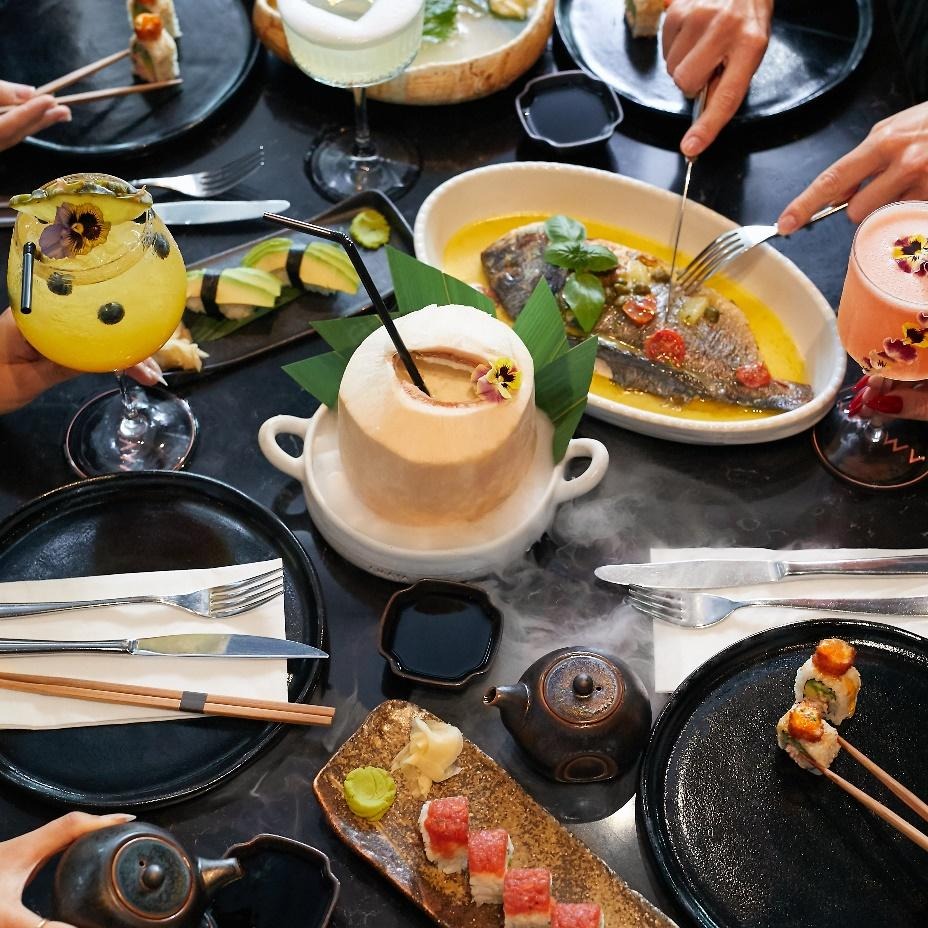 Multiple people around the table with fish, sushi, and drinks on the table