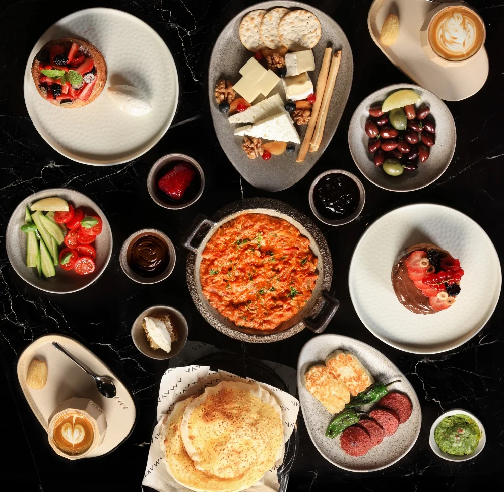 Elegant breakfast spread at AMAYA Dubai Mall featuring Mediterranean dishes, fresh fruits, cheeses, olives, pastries, pancakes, dips, and artisan coffee in a luxury fine dining setting.