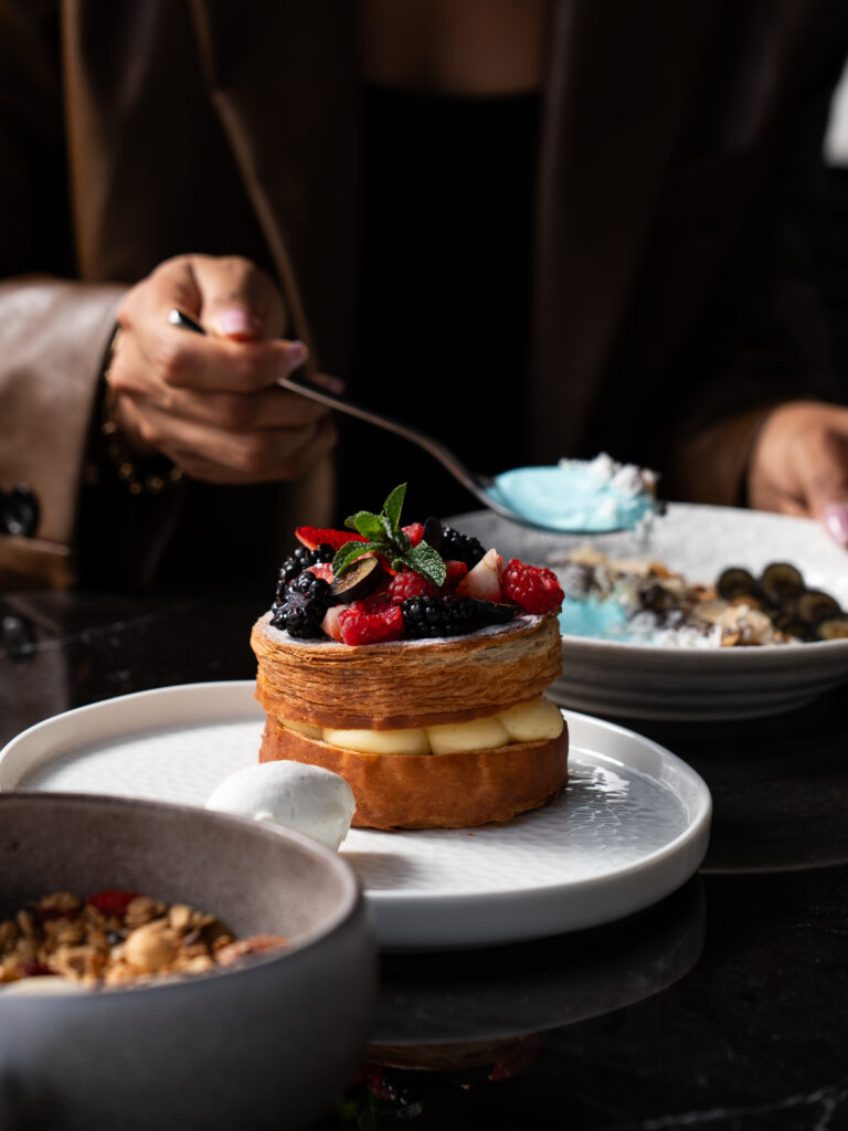 Elegant berry pastry dessert topped with fresh raspberries, blackberries, and mint on a white plate at a fine dining restaurant table.